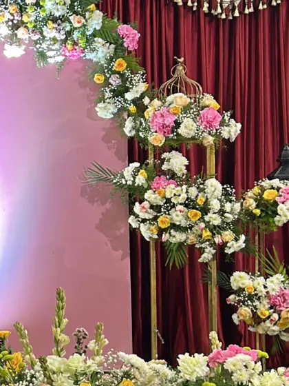 Beautiful tiered floral arrangements on golden stands, adding a touch of elegance to a celebration with a red curtain backdrop.