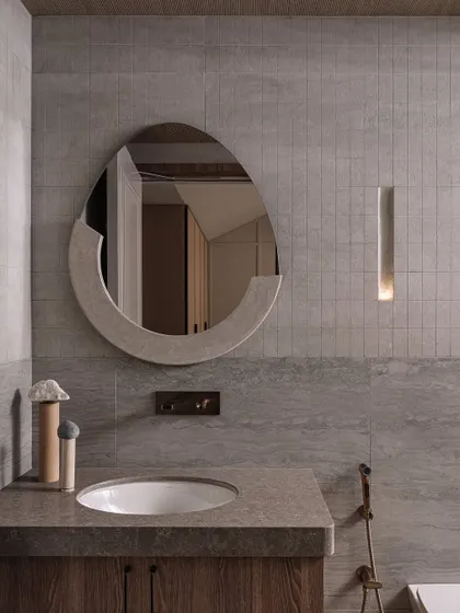 The guest bathroom continues the theme of functional art. A custom-shaped mirror and a sleek, inset light fixture glow with a muted vibe, proving that even utilitarian spaces can be sources of beauty.