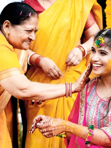 A heartwarming moment of a mother applying Haldi to the smiling bride, full of love and tradition.
