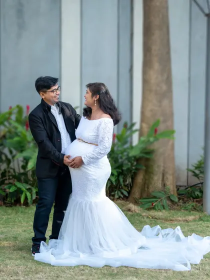 A happy couple portrait in a park. The mom-to-be looks radiant in a white mermaid-style gown.