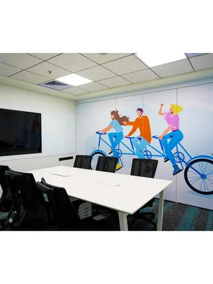 This meeting room at Mindsprint features a playful wall mural of a tandem bicycle, symbolizing teamwork. The simple furniture and large screen make it a functional space for collaborative project work.