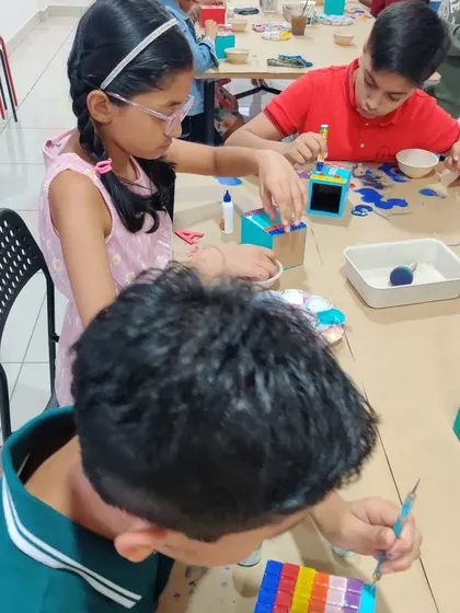 Kids are deeply focused on decorating their pen stands with colorful mosaic tiles and paint.
