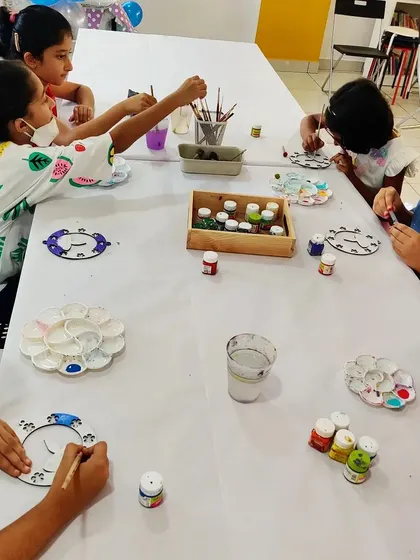 A table of young artists painting clock-like Diwali decorations during a festive birthday party.