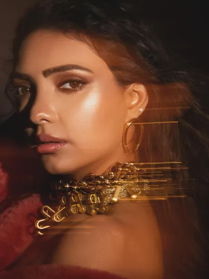 An artistic shot with a light trail effect, adding a dynamic and modern twist to a beauty portrait. The styling focuses on a statement gold necklace and glowing makeup.
