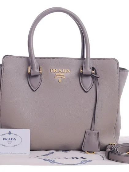 The handbag is displayed with its dust bag, authenticity card, and strap, providing a complete product view for a potential buyer.