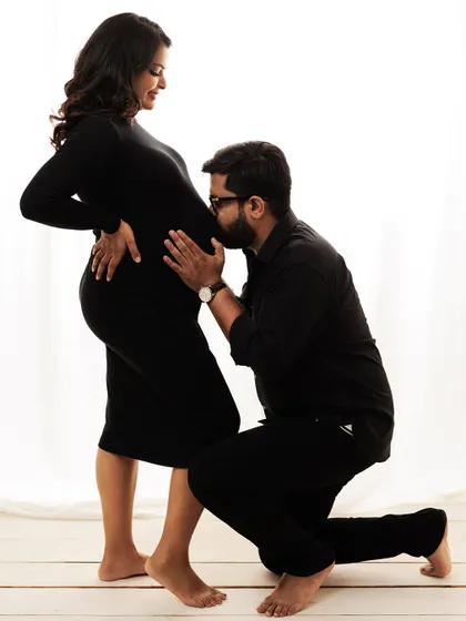 A beautiful and classic maternity pose, with the dad-to-be kneeling to kiss the baby bump. A timeless expression of love and anticipation.