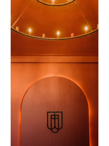 This image showcases the restaurant's branding integrated into the design. The logo is set against a textured, arched niche with warm backlighting, creating a memorable brand moment.