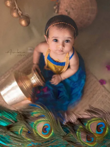 A beautiful baby girl styled as Radha, surrounded by peacock feathers and traditional elements. I use vibrant colors and authentic props to create a rich, story-filled portrait.