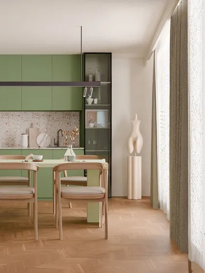 The dining area adjacent to the olive-toned kitchen echoes the same natural textures and calm palette. The simple wooden dining set and abundant natural light create a cozy, well-lit spot for everyday meals.