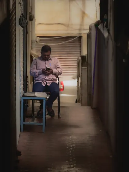 A man engrossed in his phone in a narrow alleyway. The framing and low light create a sense of privacy and isolation, even in a public space.