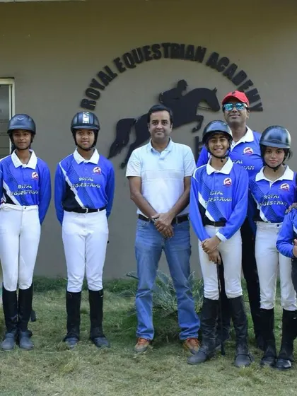 Our team posing in front of the REA logo. We are a diverse group of riders and coaches united by our love for horses and the pursuit of equestrian excellence.