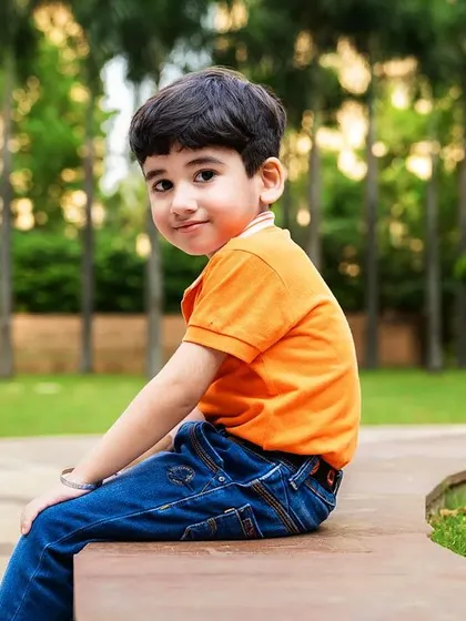 A young boy looks over his shoulder with a sweet, shy smile while sitting on a bench in a park. A lovely, candid outdoor moment.
