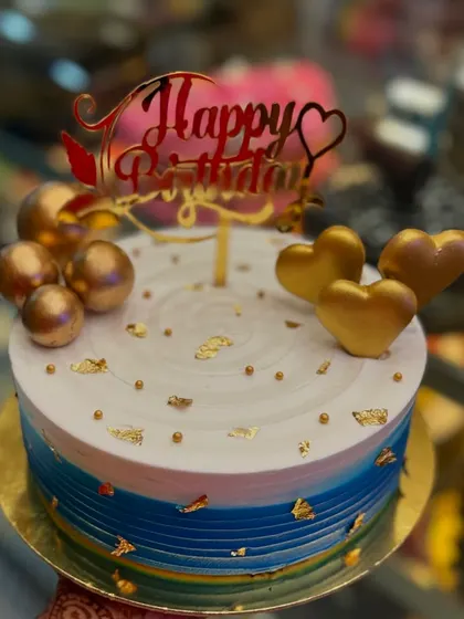A custom cake with a blue and white ombre design, accented with golden spheres and hearts. The "Happy Birthday" topper adds a final touch of celebration to this modern and stylish cake.