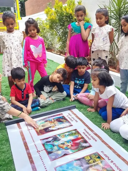 An outdoor storytelling session for Janmashtami, where children learn about the life of Lord Krishna through a large, illustrated scroll.