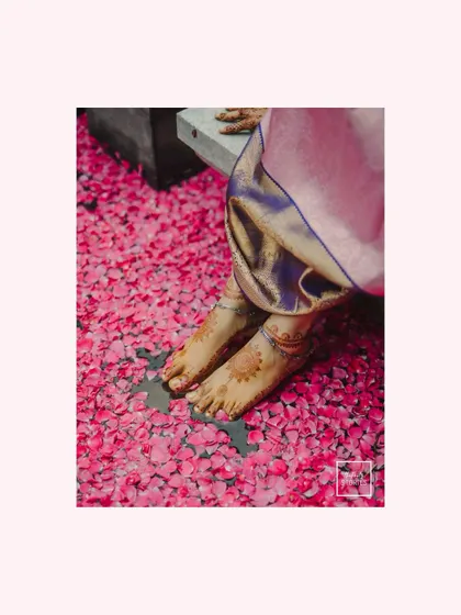 A detailed shot of the bride's feet, adorned with henna and anklets, standing on a bed of pink petals. A simple, artistic, and beautiful image.