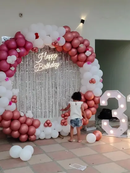 This grand backdrop for a 31st birthday includes a circular balloon arch in rose gold and white, a silver shimmer curtain for photos, a neon sign, and large light-up numbers.