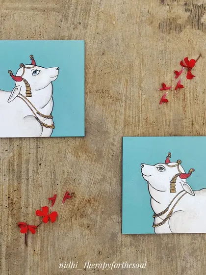 A pair of small square canvases featuring a cow painted in the Pichwai style. This art form traditionally depicts tales of Krishna, and the cow is a beloved and sacred subject.