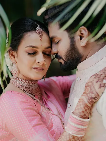 An intimate and serene portrait, with the couple's foreheads touching. The leaves in the foreground add a layer of depth and a sense of privacy.