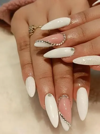 A glamorous white manicure on stiletto nails, featuring glitter accents and a sweeping line of rhinestones.