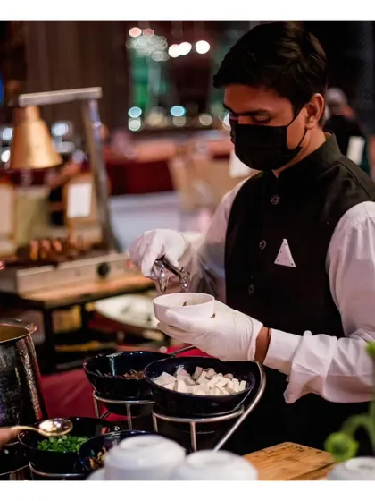 A server at our Khao Suey station, assembling a customized bowl with various toppings for a guest.