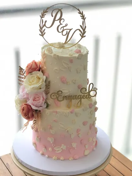 A two-tiered engagement cake with a soft pink ombre effect, delicate piping, and fresh flowers.