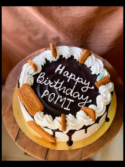A round Lotus Biscoff cake with a chocolate drip and whipped cream swirls.