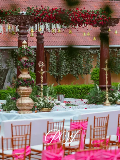A detailed view of our traditional mandap setup, featuring stacked brass pots (kalash) with floral arrangements, polished wooden pillars, and a canopy of red roses.
