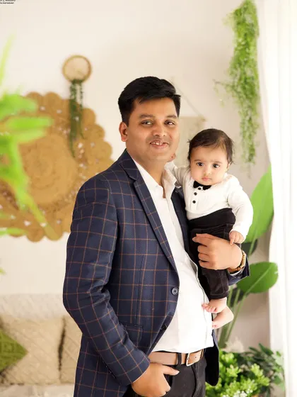 A proud father holding his baby boy, who is dressed in a smart tuxedo-style outfit. A lovely portrait from a family session.