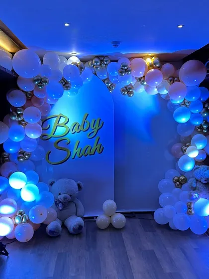 A beautiful baby shower backdrop with an arch of blue-lit balloons, creating a magical and ethereal glow for an evening celebration.