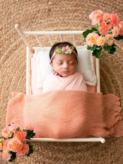 Another angle of the newborn in a miniature bed, showing the full setup with a peach blanket and floral accents.