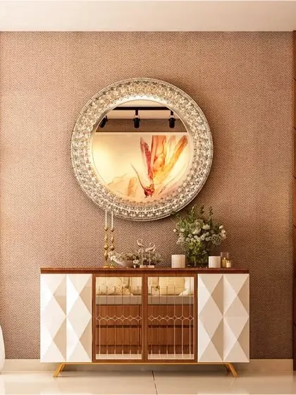 A sophisticated console unit in a dining or foyer area. The design features a cabinet with a 3D geometric pattern, chevron wood paneling, and a large, crystal-embellished circular mirror.