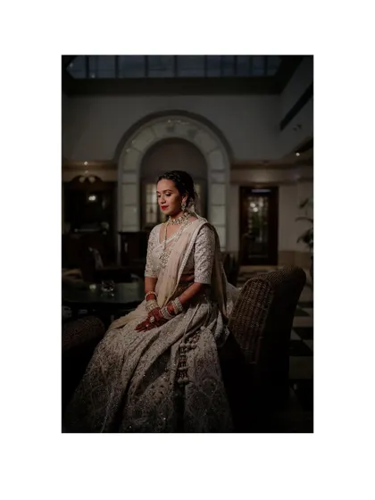 A full-length version of the elegant, seated bridal portrait. The dramatic lighting and classic setting create a sophisticated and timeless image that feels like it belongs in a luxury magazine.