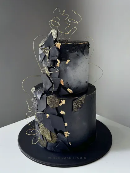 Black and gold never go out of fashion. This modern, two-tiered cake features a dramatic black concrete texture with gold leaf and abstract geometric shards.