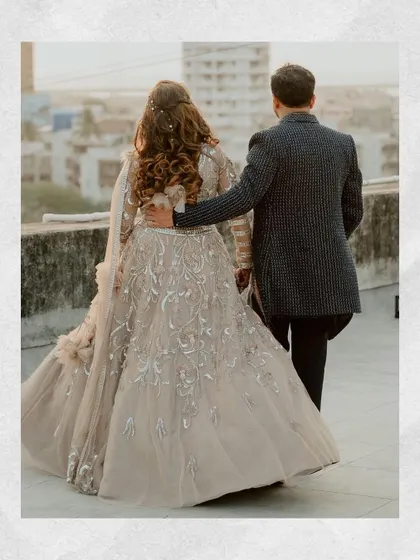 A classic walking shot from behind, highlighting the beautiful details of the bride's lehenga and the couple's connection.