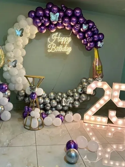 A glamorous 25th birthday with a purple, white, and silver theme. This setup includes a circular balloon arch, a neon sign, and large light-up numbers.