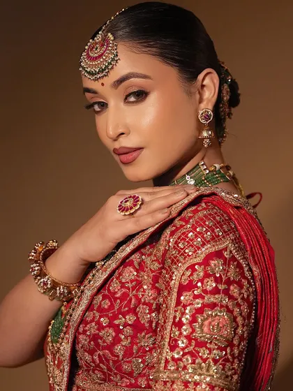 A regal and glamorous look with hazel eyes, soft glam glittery eyeshadow, and a glow that perfectly matches the red and green bridal lehenga.