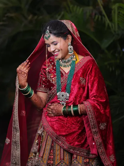 A candid moment of bridal joy. This bride looks absolutely beautiful in her red velvet lehenga, complete with stunning green bridal jewellery.
