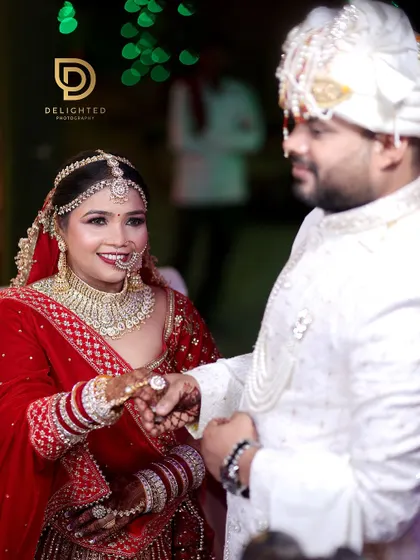 A happy moment during the wedding ceremony where the bride smiles brightly at her groom, showcasing her stunning red lehenga and intricate jewelry.