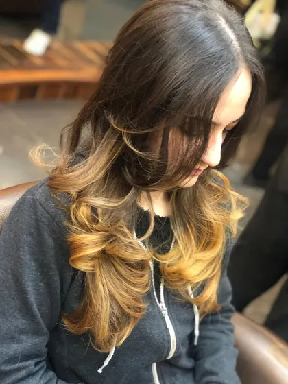 An ombre effect with a dark base transitioning to warm, golden ends. The hair is styled with layers and curls to blend the colours seamlessly.