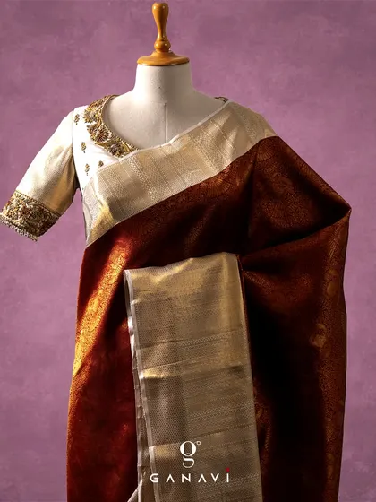 A stunning combination of a deep maroon silk saree with a contrasting ivory blouse. The blouse features intricate gold and maroon embroidery along the neckline and sleeves, offering a sophisticated and unique color palette for a bridal or festive occasion.