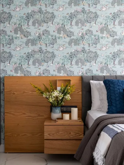 A master bedroom in a Jaipur penthouse, designed as a cool retreat from the heat. The ethereal wallpaper depicts serene Indian countryside vistas, complemented by a wooden headboard and fresh flowers.