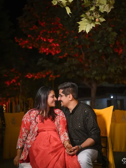 A romantic evening shot of the couple during their Mehandi function, framed by beautiful red leaves and bokeh lights.