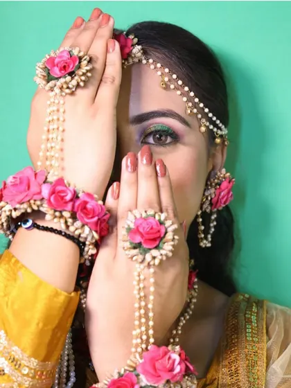 An artistic close-up of a model wearing a complete floral jewellery set. This shot highlights the hath phool (hand harness), rings, and maang tikka made of beautiful pink roses and pearls.