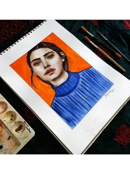 An angled view of the orange and blue portrait, showing how it looks in a sketchbook format before being framed.