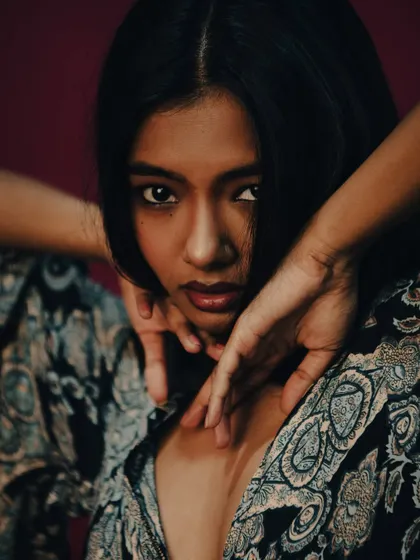 An intense and captivating close-up, with the model's hands framing her face.