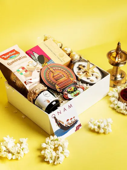 The 'Jamanthi Poo' Onam hamper, a bright and cheerful collection. It includes sweet and savory treats, a scented candle, and a Kathakali magnet, all set against a vibrant yellow backdrop symbolizing prosperity.