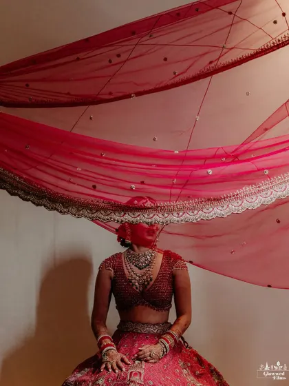 An artistic portrait of the bride, her face covered by her flowing red veil, creating a sense of mystery and elegance.
