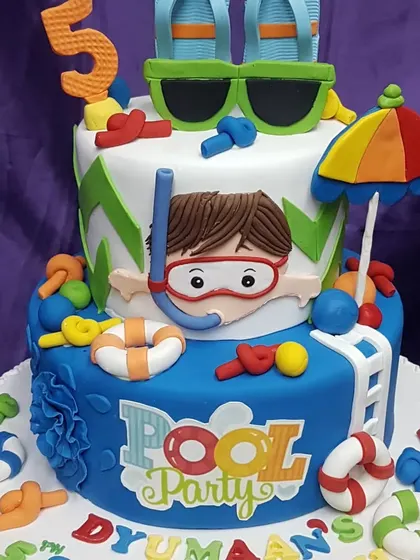 Time for a pool party! This fun, two-tier cake is decorated with everything you need for a day by the water, including sunglasses, flip-flops, and a snorkeler ready to dive in.
