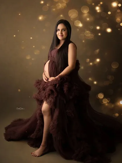 Surrounded by a warm, golden bokeh, this mom-to-be shines in her dark brown ruffled gown.