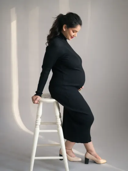 A full-length profile portrait in a sleek black dress, highlighting the graceful curve of her pregnancy. This image has a modern and sophisticated feel, celebrating the strength and beauty of the female form.
